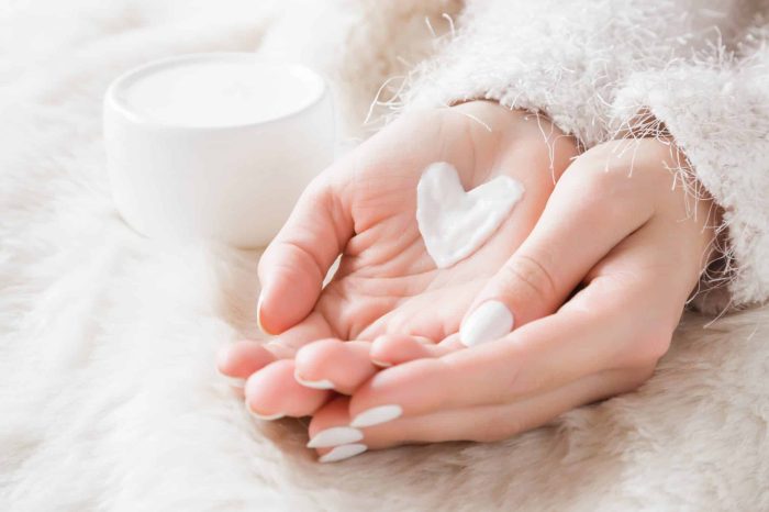 Beautiful groomed woman's hands with cream jar on the fluffy bla